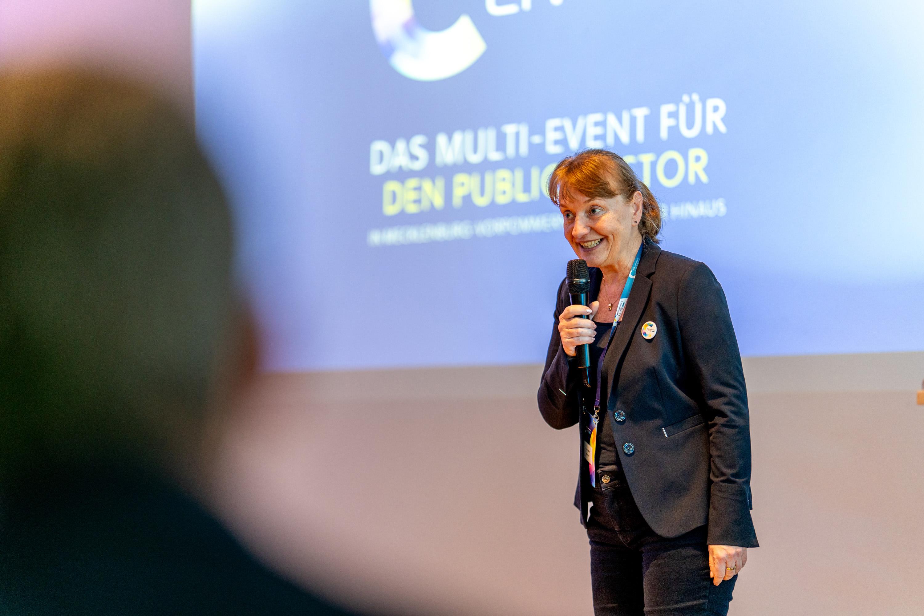 Uta Knöchel spricht auf der Bühne, lächelt und trägt ein dunklen Blazer.
